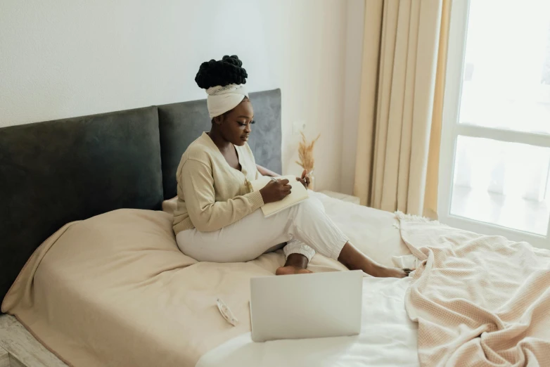 a woman is sitting on a bed while using her laptop