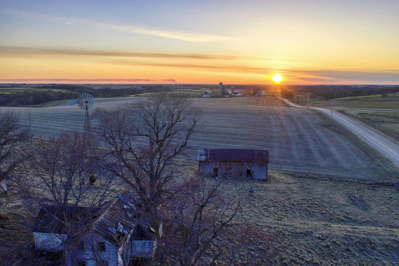 the sun setting over a rural land and a small house