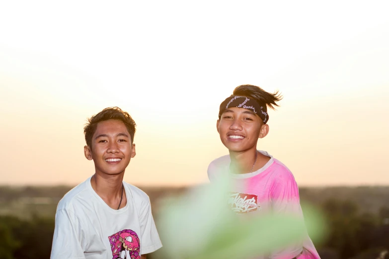 two young men, one of whom is wearing a pink shirt, are smiling