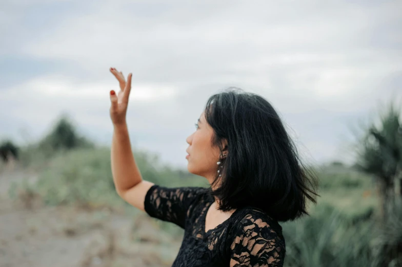 a young woman in a black lace dress and earrings is blowing a candle outside