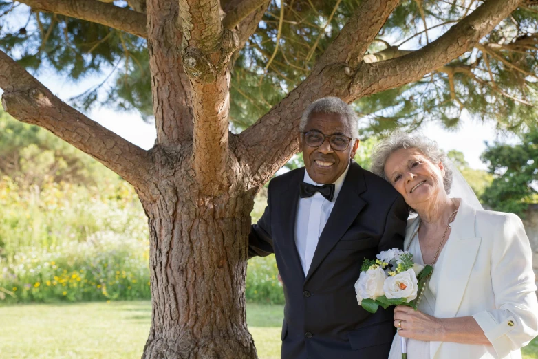 an older couple emcing near a tree for a wedding