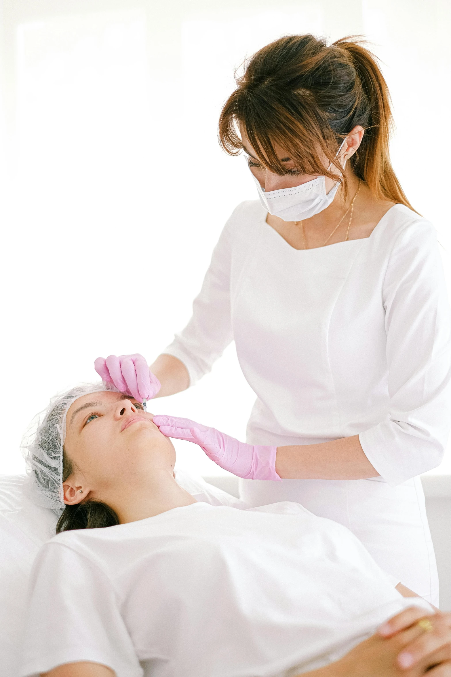 woman in pink gloves and mask tending to older women in white gown