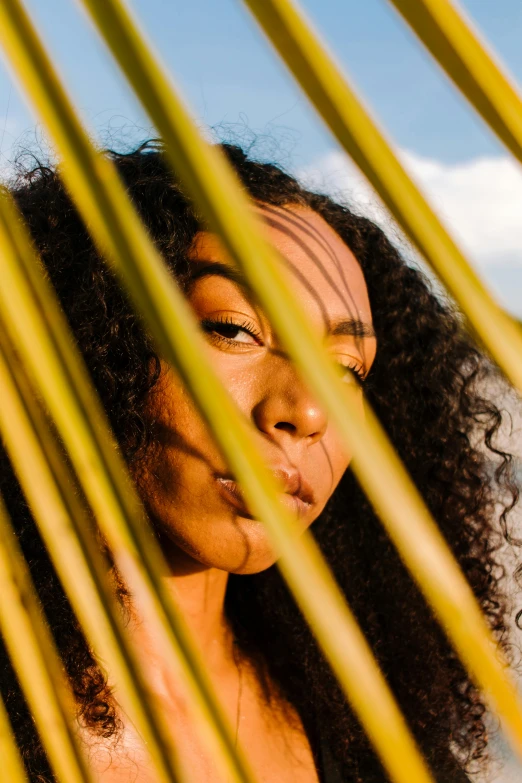 a woman with long dark hair is looking through yellow thin stalks