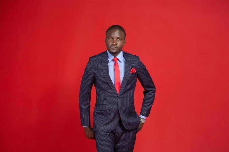 a black man in a suit and tie standing against a red backdrop