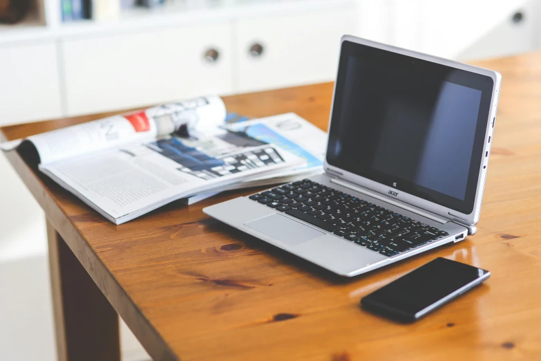 an open laptop sits on the table with magazine and phone