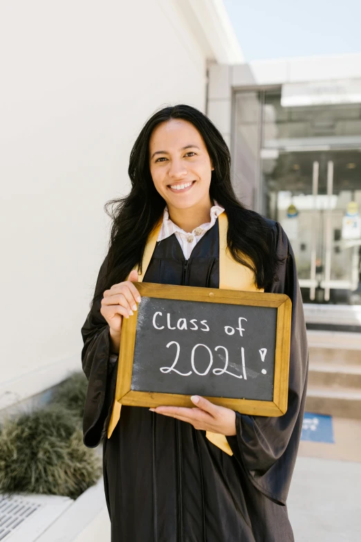 a woman in a graduation gown holding up a sign