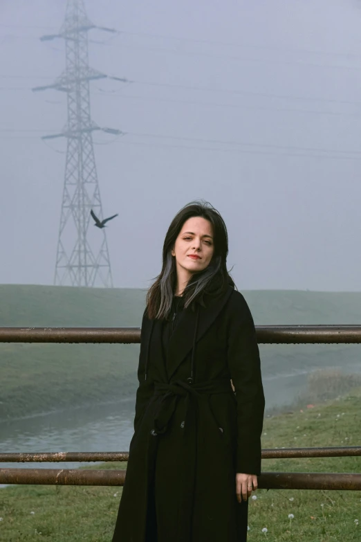 a woman standing next to a metal fence near a hill