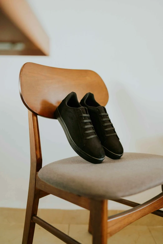 a black pair of sneakers is seen on top of a wooden chair