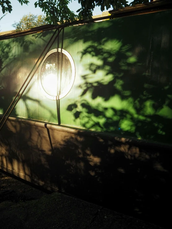 the sun shines on a large green wall and shadows of trees