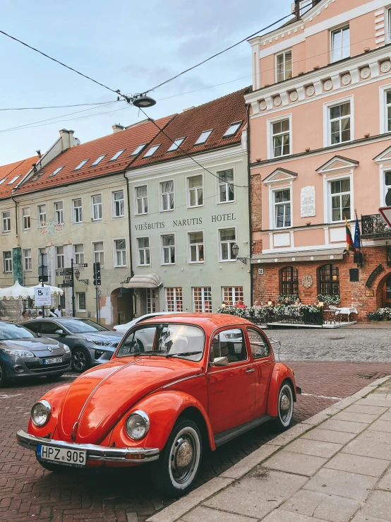 small orange car parked near many buildings on the side of a street