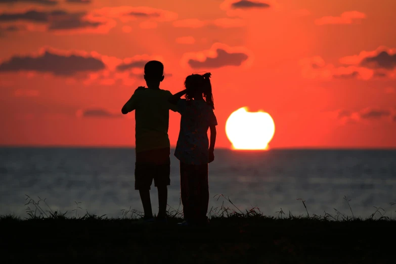 two people on a hill facing the ocean during a sunset