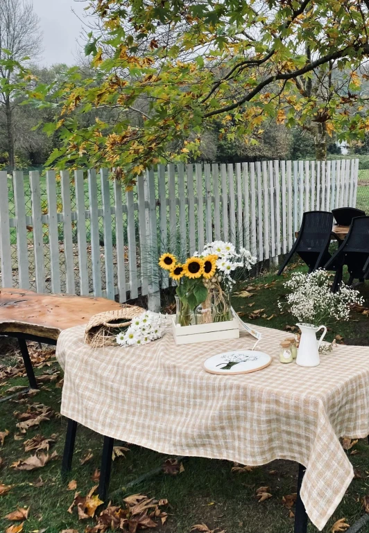 a picnic table set outside with sunflowers and flowers