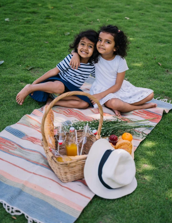 two girls are sitting on the grass with a picnic blanket