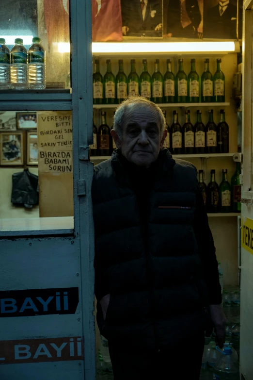 an older man stands in front of a small fridge with drinks