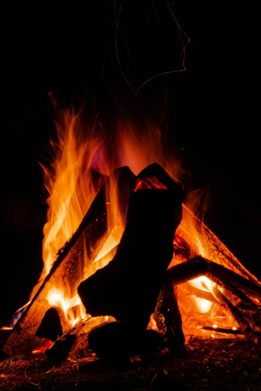 a fire burns brightly at night while someone sits in front of it