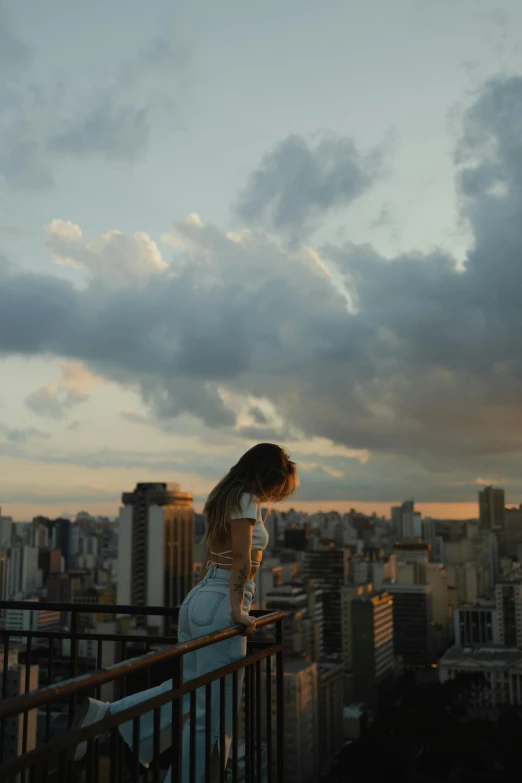 a woman drinks from a wine glass while standing in a balcony overlooking the city