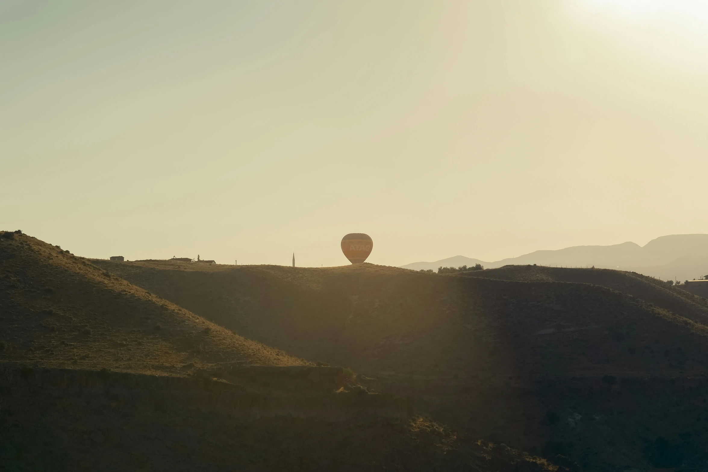 the sun shining behind the balloon above some hills