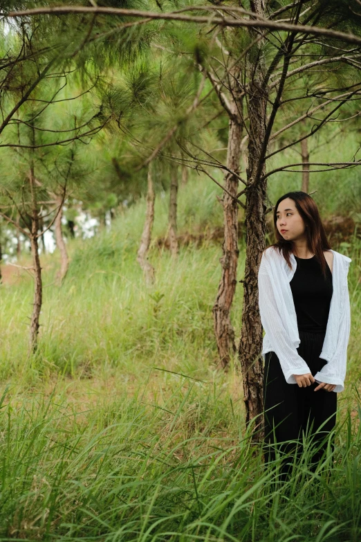 a woman is standing in tall grass by some trees