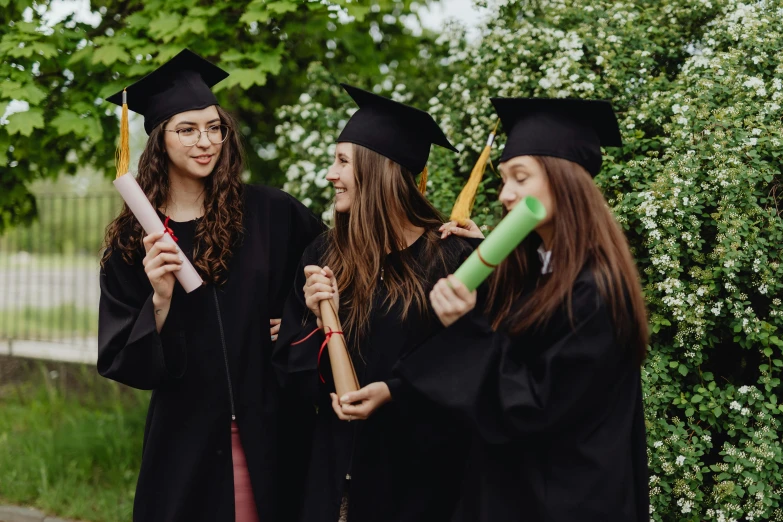 three women in graduation hats and gowns hold diplomas