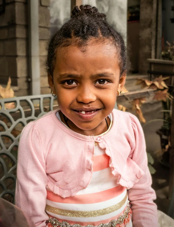 a little girl smiles in a pink top with a white and gold stripe