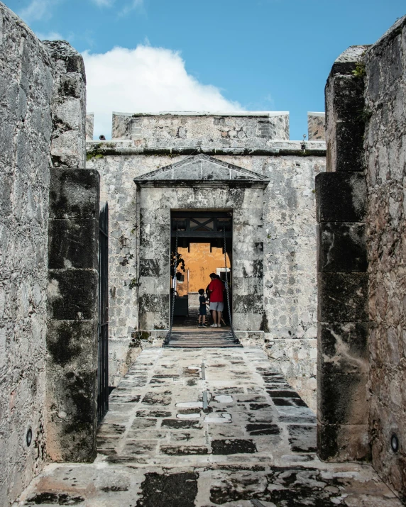 people entering an old stone walled courtyard with a sky background