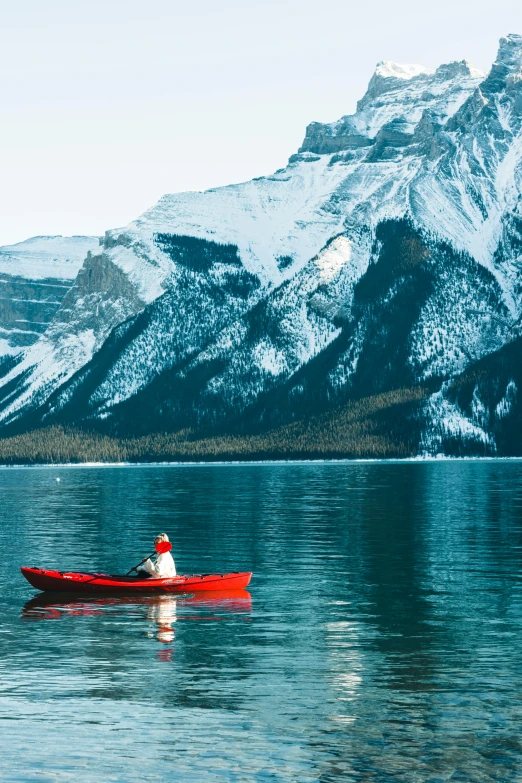 man paddling in a red canoe on mountain lake