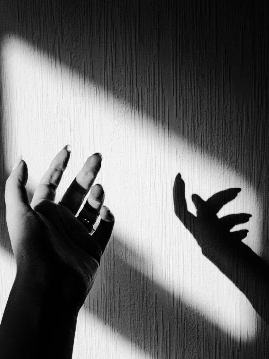 a hand reaching up towards the light coming through a shadow door