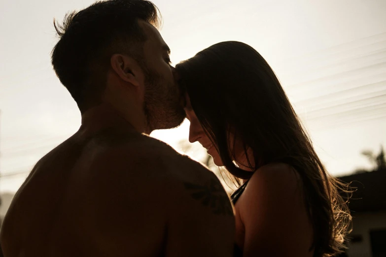 an attractive couple standing in the dark in front of a sunset