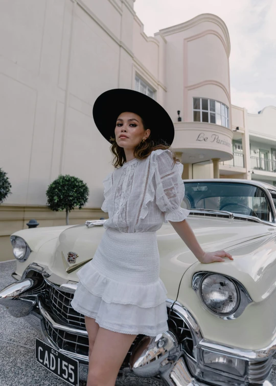 woman in white dress with a big black hat and boots by a car