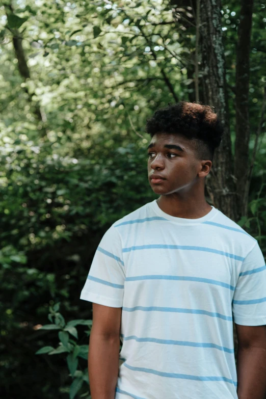 a young man standing in front of trees in a forest