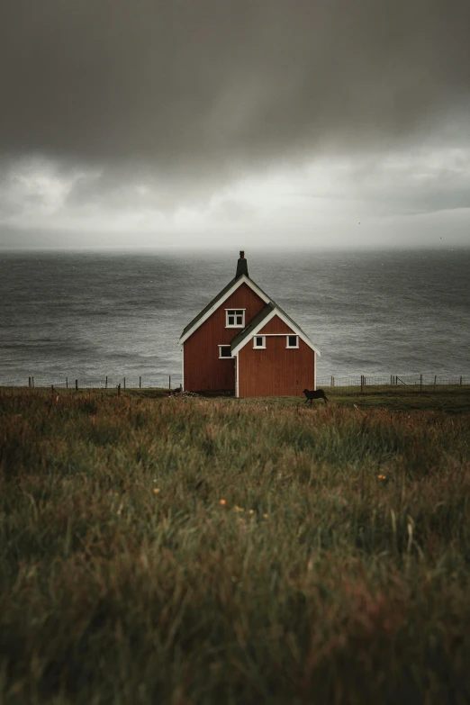 a red barn next to the ocean with a cloudy sky