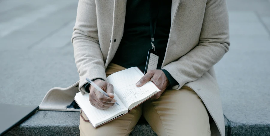 the man is sitting down and writing on his notebook