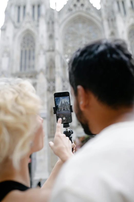 a woman holding her cell phone and taking a picture of a man with cathedral