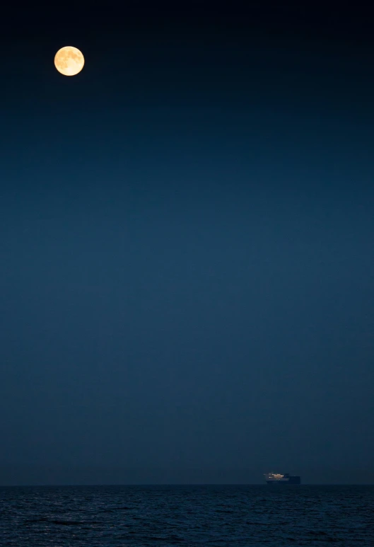 the moon is reflecting over the ocean and a boat in the distance