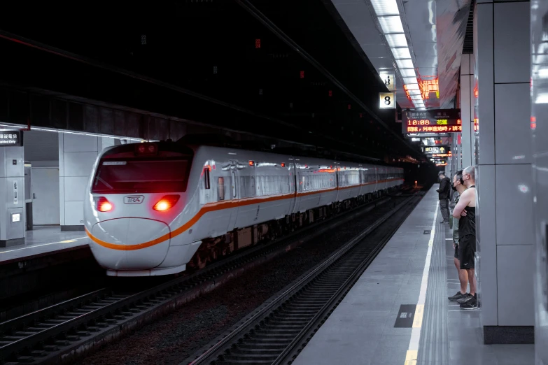 a train pulling up to the platform with it's lights on