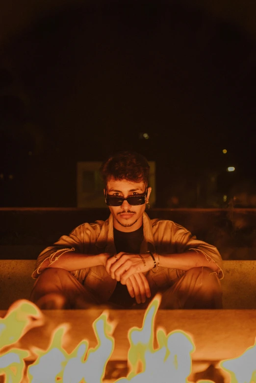 man with sunglasses sitting near fire and flames in the ground