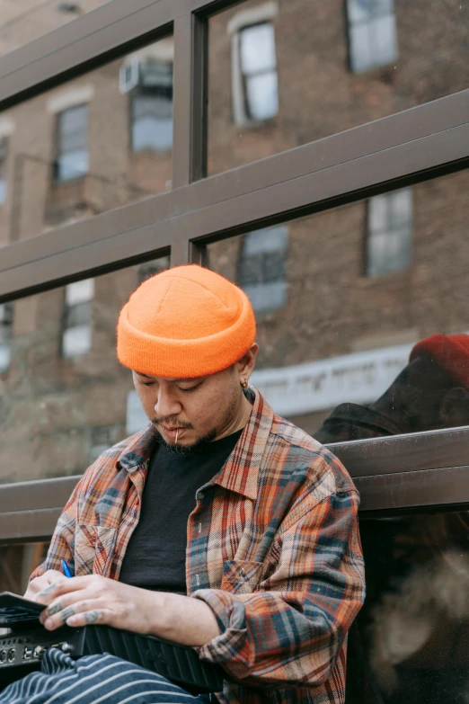 man wearing orange knitted hat sitting on bench with a digital tablet