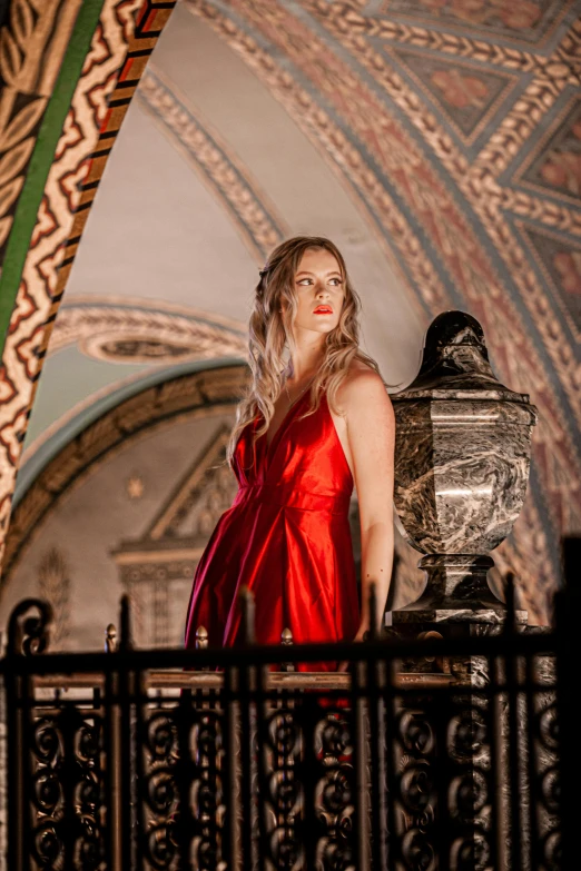 a young woman in a red dress stands on a railing by an ornately painted archway