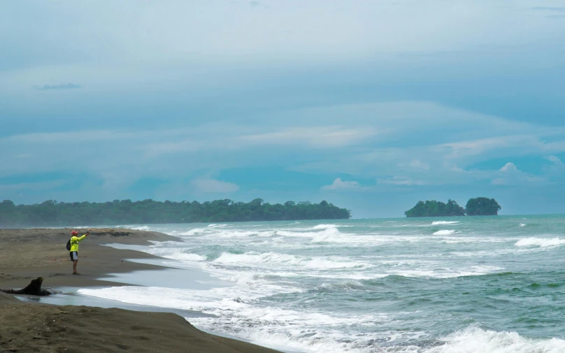 a man with a yellow jacket is walking on the beach