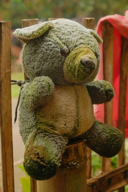 a green teddy bear sitting on top of a wooden pole