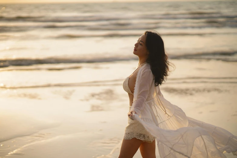 a woman on the beach with her long dress blowing in the wind