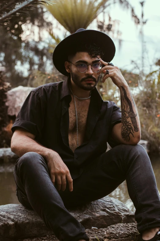 a man with a hat and glasses is sitting by the river