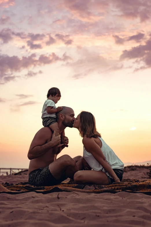 the man kisses the baby and kisses it while a woman holds the child on his shoulders