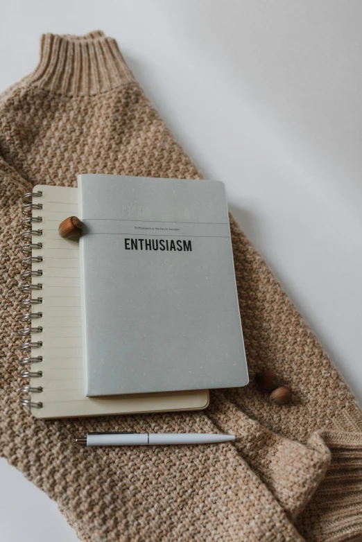 a notebook with the word enthusiasm written on it sits on a sweater