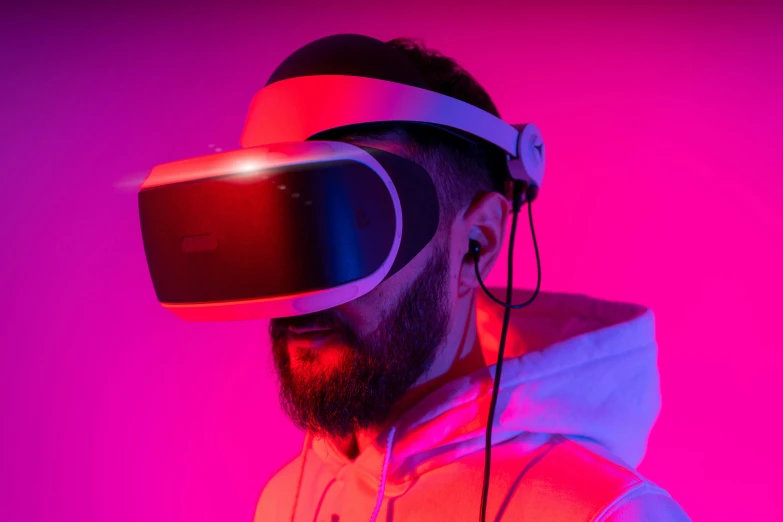 man in hooded sweatshirt wears virtual reality headset over pink background