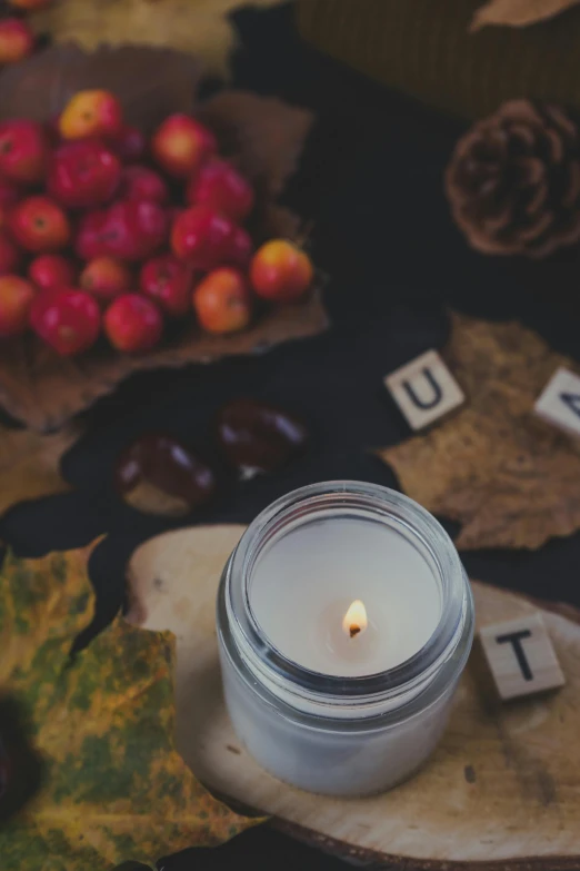 a candle sitting in a jar next to some autumn leaves