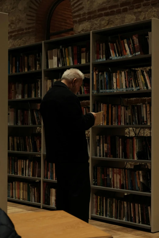 a man reading books in front of a large bookcase