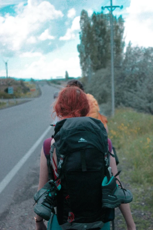 two people with backpacks walking down a paved street