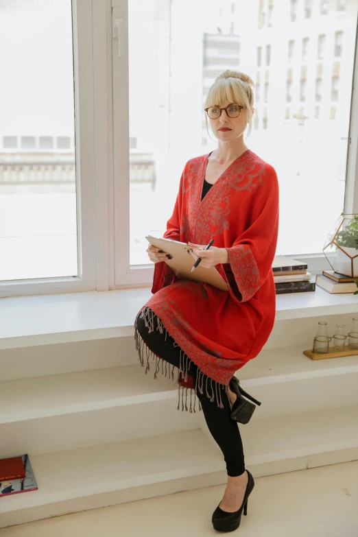 a woman wearing a red top sitting by a window