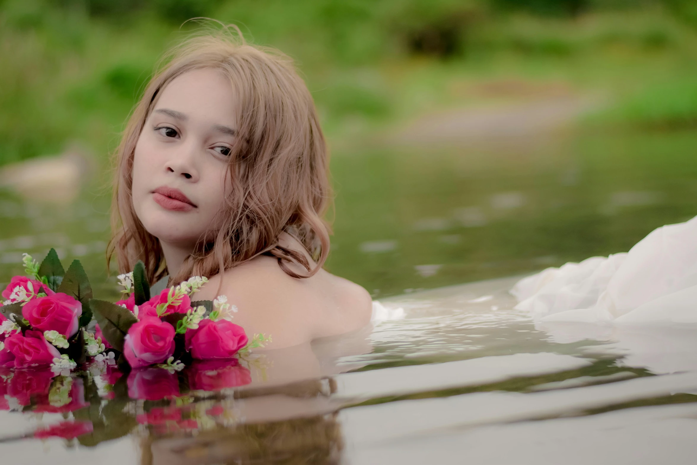 young woman with flowers sitting in a river near grass